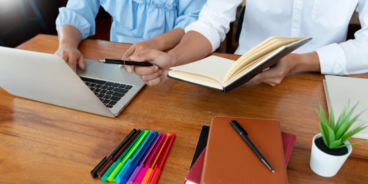 Lehrkräfte arbeiten gemeinsam an einem Laptop mit einer Schulverwaltungssoftware in einem geteilten Arbeitsbereich.